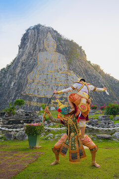 Traditional Thai Khon masked dancers performing a Ramayana scene in front of the giant Buddha image carved on the mountain at Khao Chi Chan Buddha Image. Cultural performance in traditional Thai costu