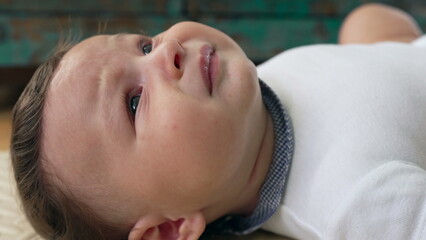 Baby lying down with furrowed brows, mouth slightly open, showing discomfort, uneasy expression, tense face, moment of distress, emotional reaction, indoor home setting