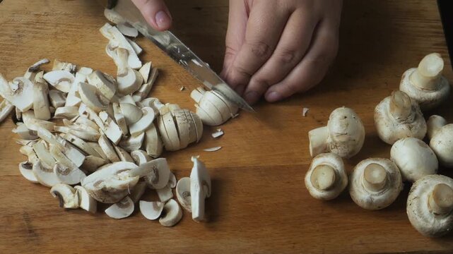 Cutting fresh mushrooms with a knife on a cutting board on a wooden table. Close-up.