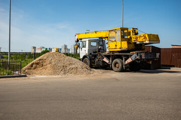 Obraz premium Crane truck on construction site next to a gravel pile and city buildings