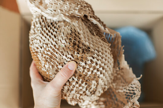 Close-up of a hand holding honeycomb kraft paper protective packaging. The expandable paper wrap with a textured honeycomb structure is used as an eco-friendly alternative to plastic bubble