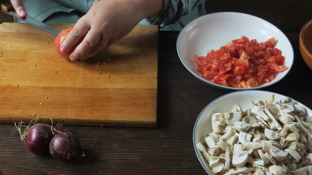 A woman's hands cut fresh red tomatoes with a knife on a cutting board on a table. Medium shot.