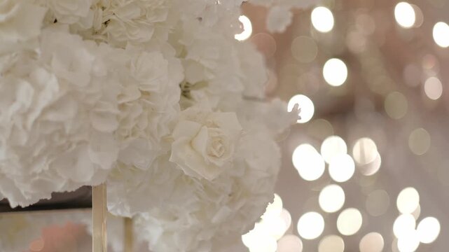 Elegant white floral arrangement with roses and hydrangeas against a warm bokeh background
