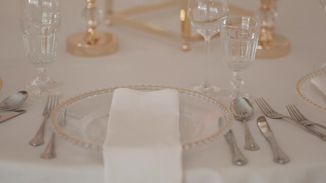 Elegant formal table setting with glass plates, silver cutlery, and crystal glassware on a white tablecloth