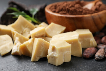 Organic cocoa butter, beans, powder and green leaves on black table, closeup