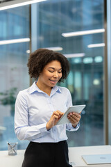 Vertical photo of a smiling young African American businesswoman in the office using a tablet