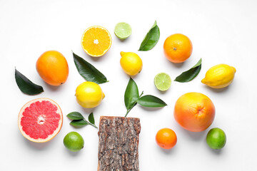 Naklejka premium Different fresh citrus fruits, green leaves and tree bark on white background, flat lay