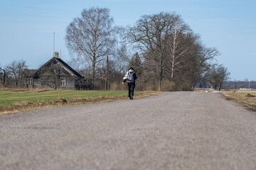 Obraz premium Person walking alone along quiet rural road near old wooden farmhouse and bare trees in countryside landscape