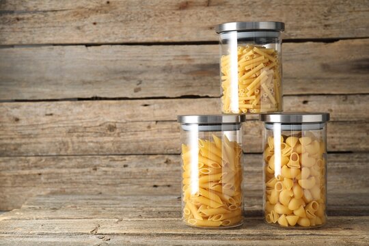 Different types of pasta in jars on wooden table, space for text