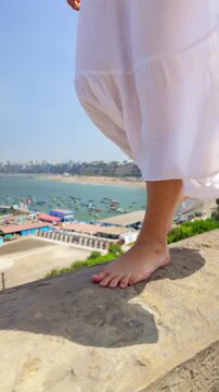 Barefoot woman walking on stone wall overlooking chorrillos bay in lima