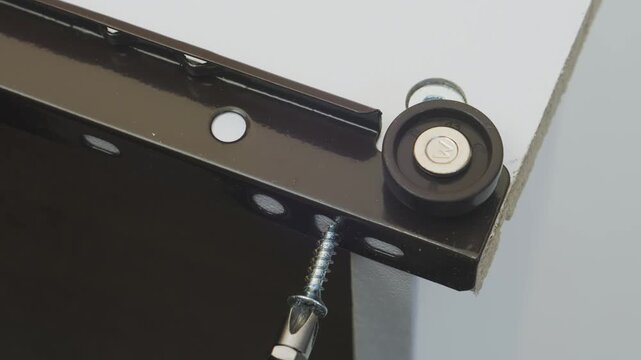 Human hands use a screwdriver to screw in the screws and assemble the furniture. The middle plan.