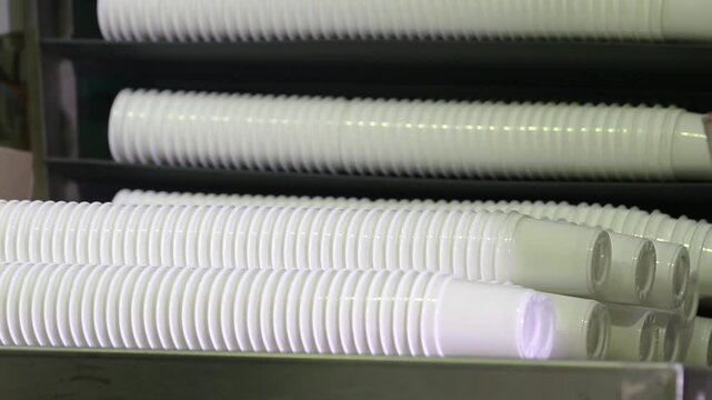 Stacks of plastic cups on conveyor belt at plastic recycling factory. Production of plastic cups for food. Worker puts plastic containers. Closeup of white plastic containers dairy products at factory