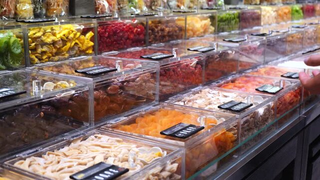 Customer's hands picking assorted dehydrated fruits from bulk bins in a supermarket. Colorful display of healthy and organic sweet snacks for sale, promoting a balanced vegan lifestyle