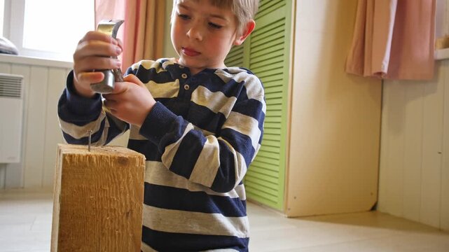 Kid hammers nails to wood with a hammer. Little boy helping with toy tools. Funny 6 years child having fun on building. Kid hammering crafting stuff using wooden pieces. Carpentry and family concept