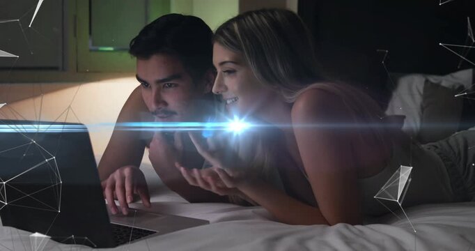 Woman pointing and man tapping laptop on bed, tech overlay brightening and leading to shared smiles
