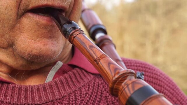 Close-up video focusing on the lips and mouthpiece as a senior musician blows air to fill the bagpipe, highlighting the texture of the wood and skin.