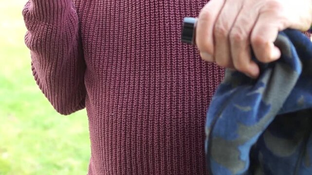 A close-up shot of an elderly man's hands removing the mouthpiece from a traditional wooden bagpipe, showing the maintenance process.