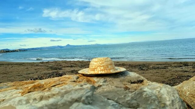 Forgotten straw hat rests on rocks by the Mediterranean Sea during a clear day