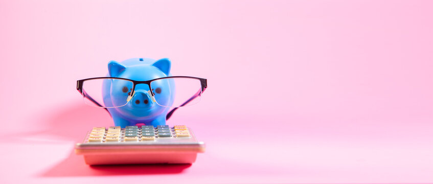 Piggy bank with eyeglasses and calculator on pink background