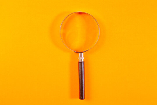 Magnifying glass on orange background. Top view. Copy space.