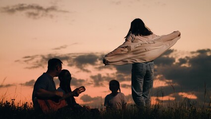 Happy family camping outdoors summer vacation. Parents children enjoy outdoors, playing guitar, singing, dancing together at sunset. Family picnic with children, singing, dancing to guitar in nature. © Victoriia