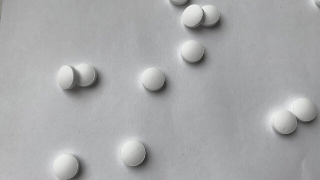 The white pills are falling, the cure for the disease. A scattering of round tablets.