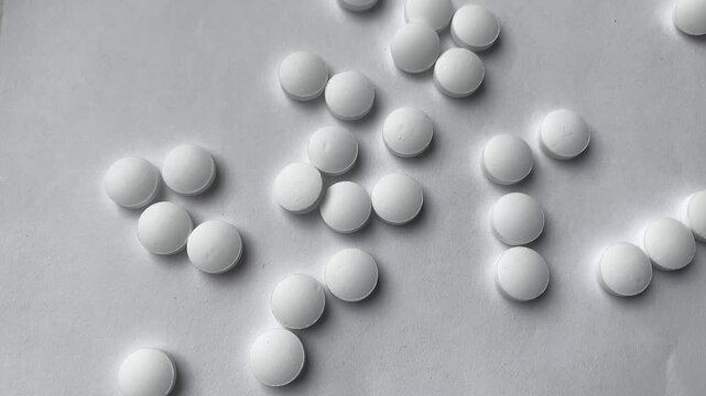 The white pills are falling, the cure for the disease. A scattering of round tablets.