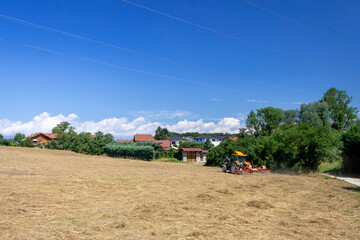 Fototapeta premium Tractor working in harvested field near rural village