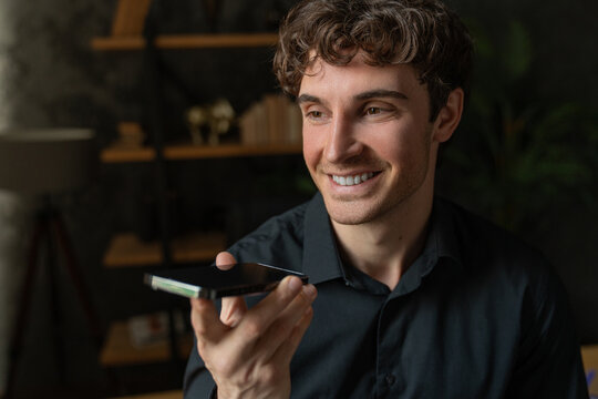 Voice application. Happy millennial male hold mobile phone talk using digital voice recorder dictate voicemail audio message. Young man enjoy tech innovation search data at web via mobile ai assistant