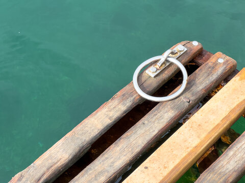 High angle close-up view of a metal mooring ring on a wooden pier over clear green sea water