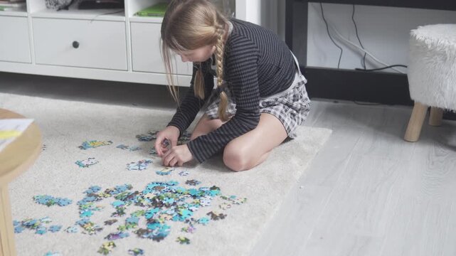 Young girl sitting on the floor solving a jigsaw puzzle at home, focused child activity and learning through play concept