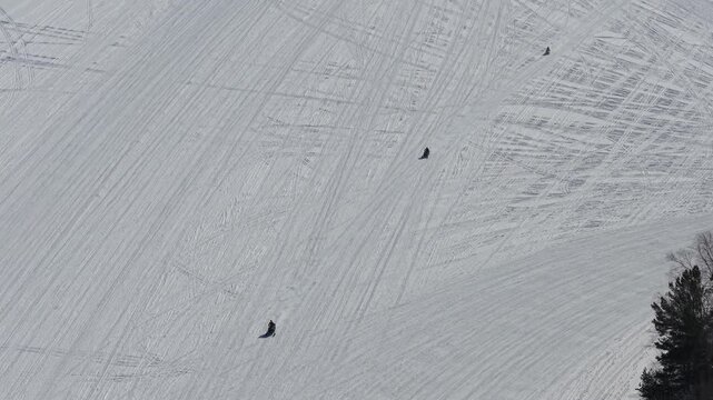 Aerial View of Four Snowmobiles on Frozen Snow-Covered Vermont Lake Riding By Stationary Drone Looking Down