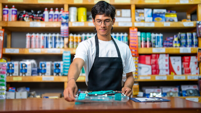 Young man wearing apron working behind cash register in a retail store