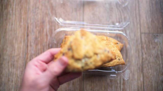 Scones, chocolate chip scone bread sweet food dessert in plastic container hand holding one biscuit macro closeup