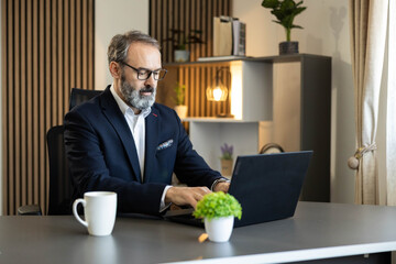 A focused man in a suit working diligently on his laptop in a modern office setting.