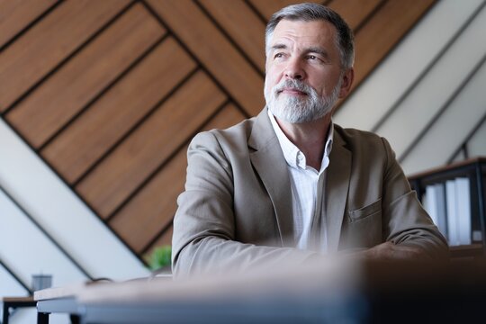 Smiling mature business man executive wearing shirt sitting at desk using laptop. Happy busy professional middle aged manager investor working on computer looking away in office