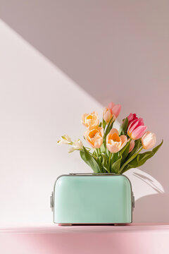 Tulips and ranunculus in a mint toaster vase on a table with slanted sunlight. Repurposed toaster holds a bouquet, bathed in warm side light. Spring, Mother's Day, Easter, home decor, minimalism.