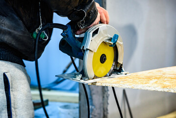 Carpenter using circular saw for cutting wooden OSB board.