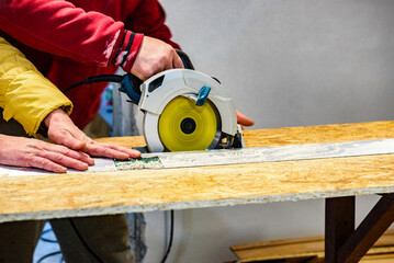Carpenter using circular saw for cutting wooden OSB board.