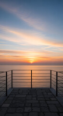 Fototapeta premium Serene sunset over the calm ocean viewed from a stone paved promenade with a metal railing creating a peaceful and picturesque coastal vista