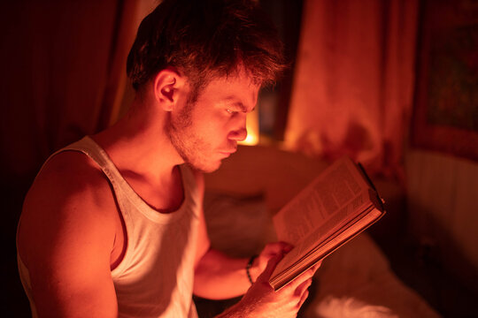A man in bed reading a book in warm light before going to sleep
