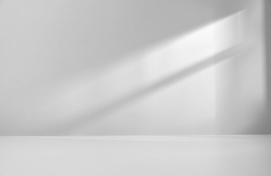 Minimalist abstract empty room with soft natural light casting a shadow on a wall. Clean, modern interior space for product presentation, with a beam of light falling into the room through the window