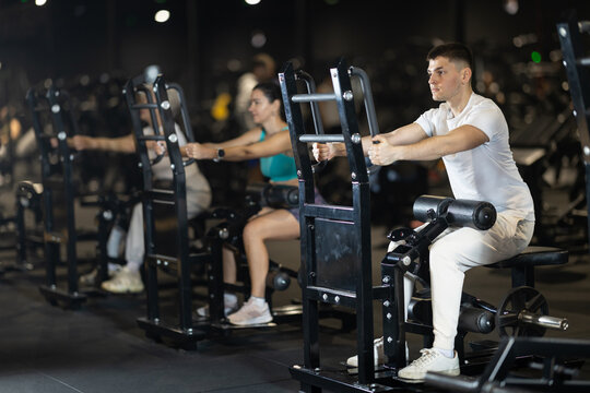 Focused athletic young man training in modern gym, finishing leg day with resistance sit-to-stand reps on machine to add volume and isolate lower body muscles..