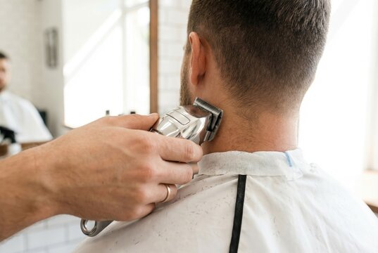 Barber using silver electric clippers to shave the hair on the back of a male customer's neck