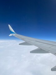 Modern commercial airplane wing flying high above white fluffy clouds under a clear deep blue sky during a daytime flight journey for travel and business concepts.