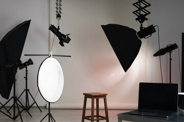Professional lighting equipment hanging from ceiling and chair in photo studio