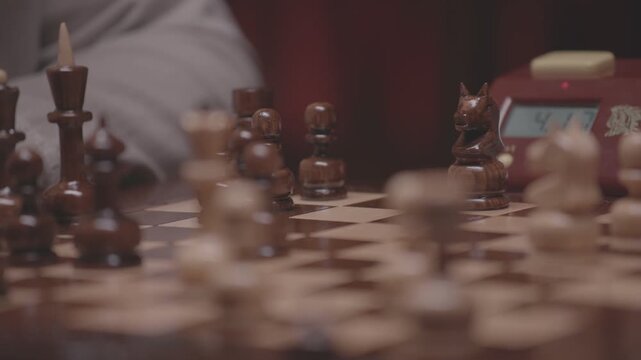 Two focused players are engaged in an intense game of chess. The camera captures a detailed close-up of a hand strategically moving a pawn across the wooden board.