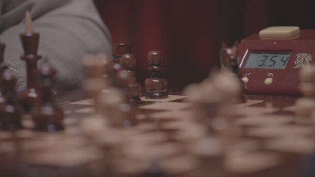 Two focused players are engaged in an intense game of chess. The camera captures a detailed close-up of a hand strategically moving a pawn across the wooden board.