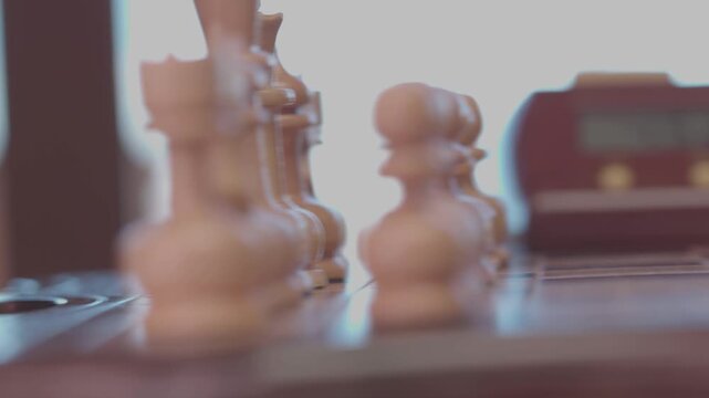 Two focused players are engaged in an intense game of chess. The camera captures a detailed close-up of a hand strategically moving a pawn across the wooden board.