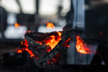 Fototapeta premium Glowing embers and charred logs burn in a modern hearth in the Dolomites. A glass fireguard reflects ambient light as a lounge scene uses shallow depth and low light.